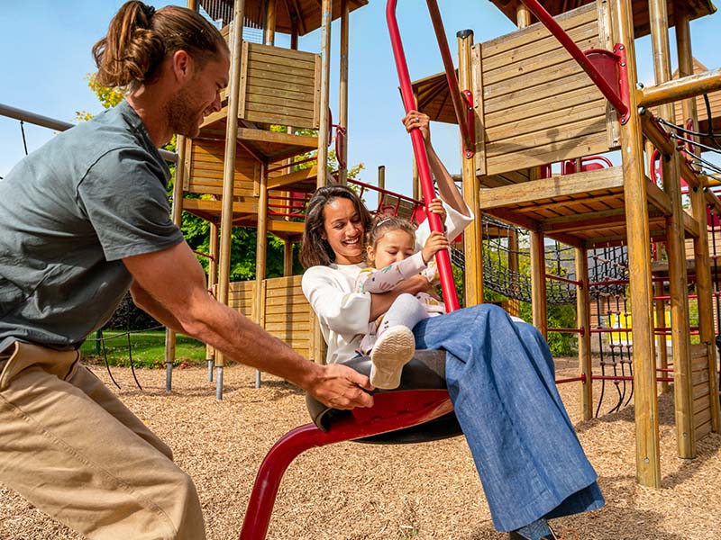 man pushing woman and child on a playground ride at emerald park