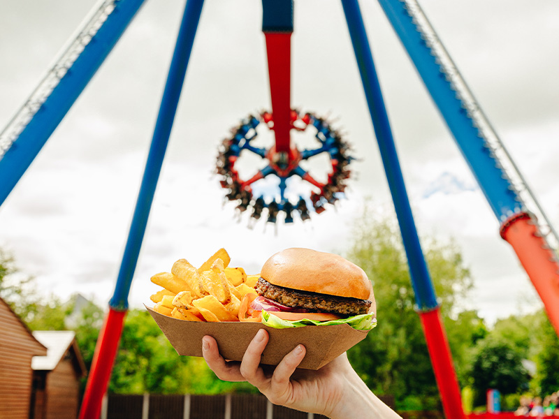 A person holding up a burger and fries basket n front of the rotator ride at emerald park