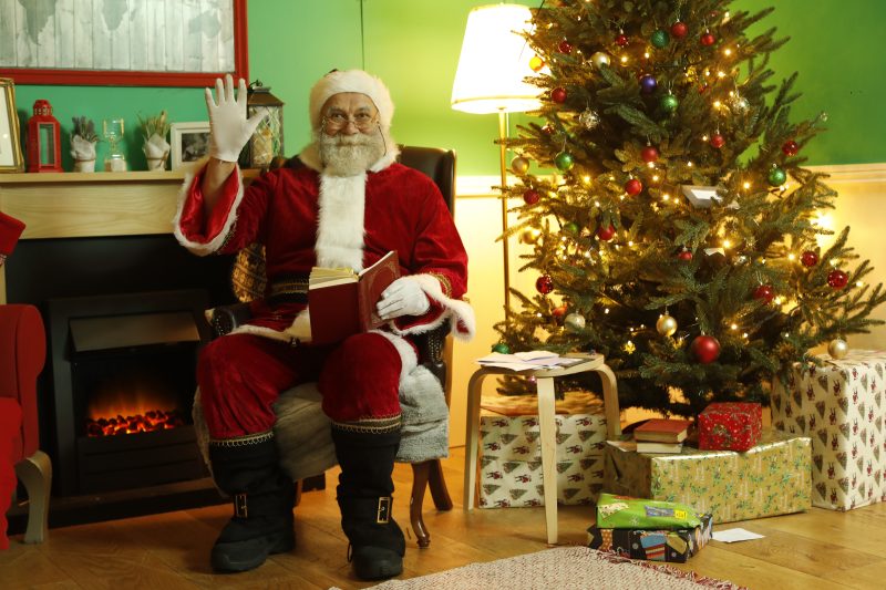 Santa clause waving while sitting down and holding a book
