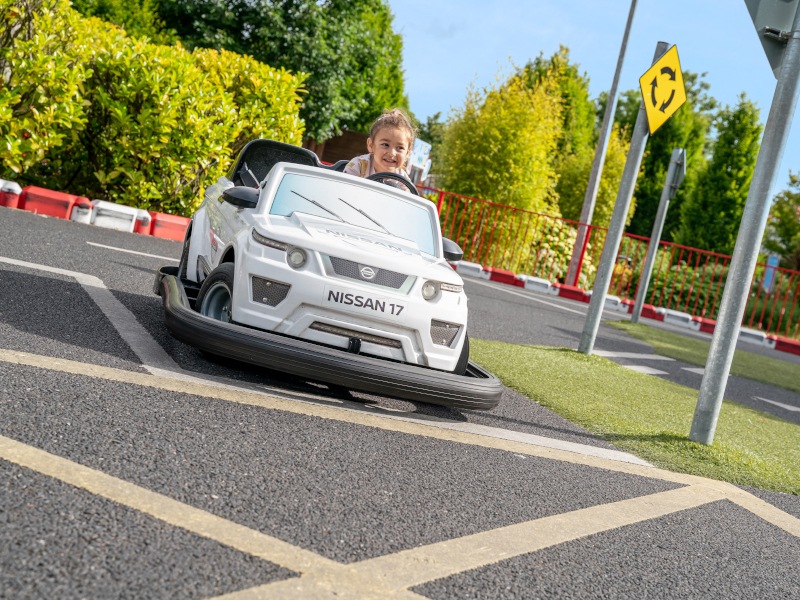 A small girl driving the child size car at the driving school area