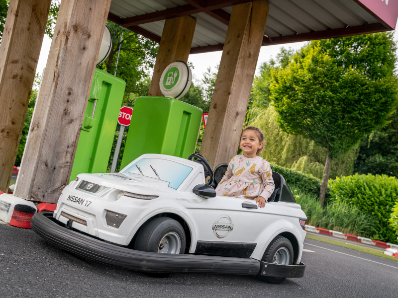 a young girl is driving a miniature automobile while happy in a close-up at Emerald Park.