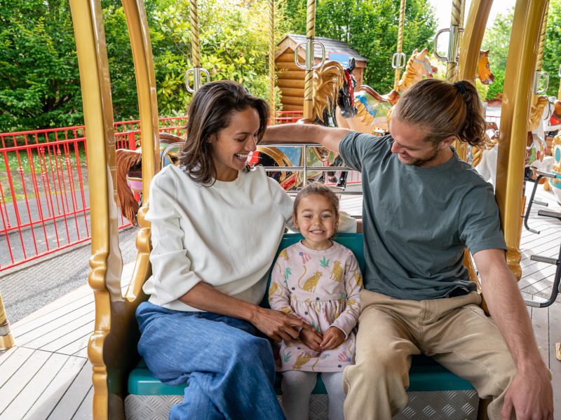 Two parents and a child are riding on the grand carousel at Emerald park.