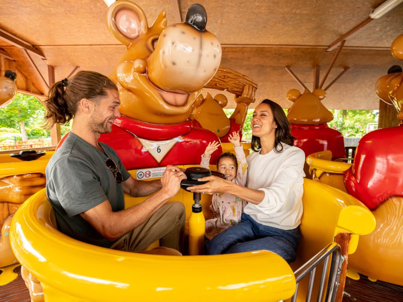 Two parents are turning the ride's wheel as a child's hands are up.