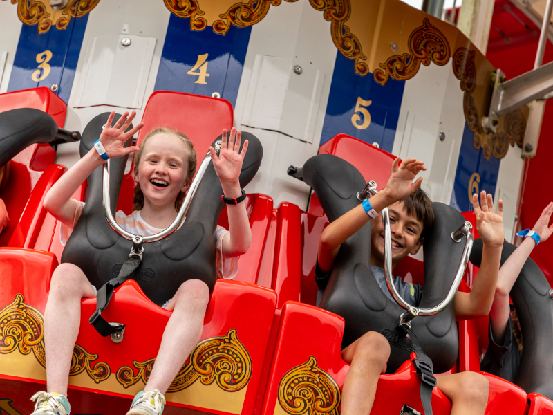 children raising hands on colourful theme park ride