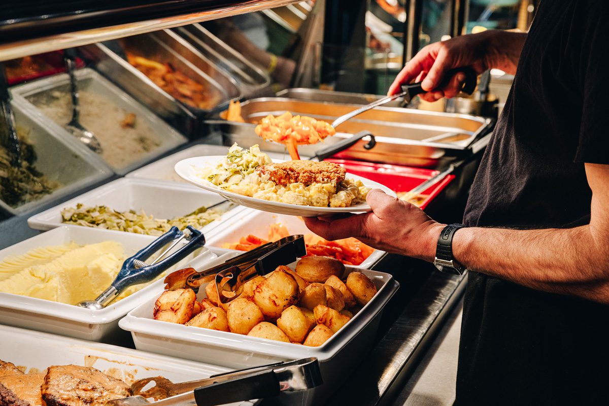 close up of hands placing food on plate in carvery restaurant emerald park