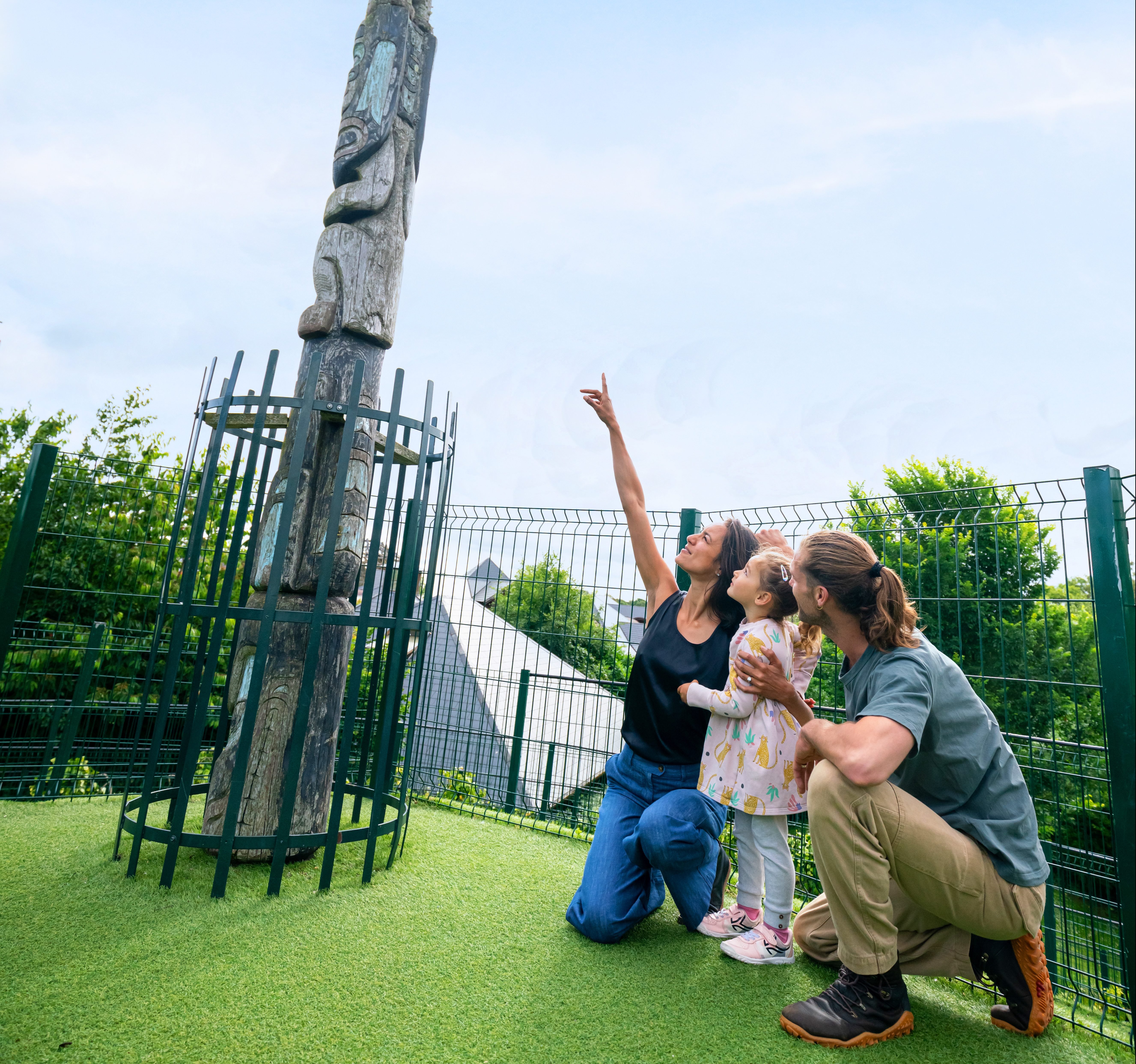 a man and woman with their child point at a totem pole