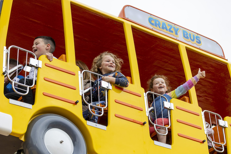a group of children smiling and enjoying a theme park attraction that is designed to look like a yellow school bus
