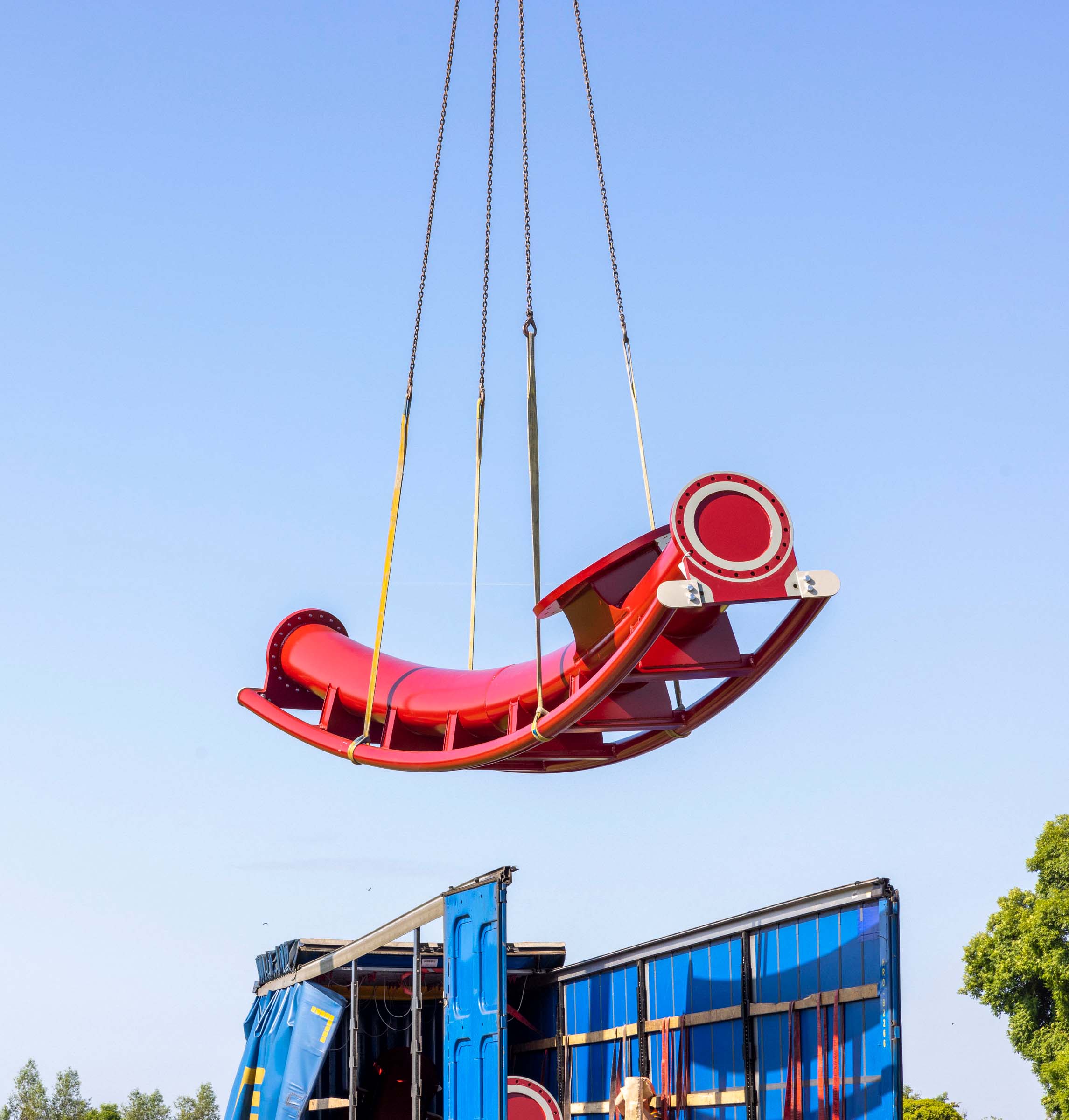 a red rollercoaster track being lifted from a truck by a crane