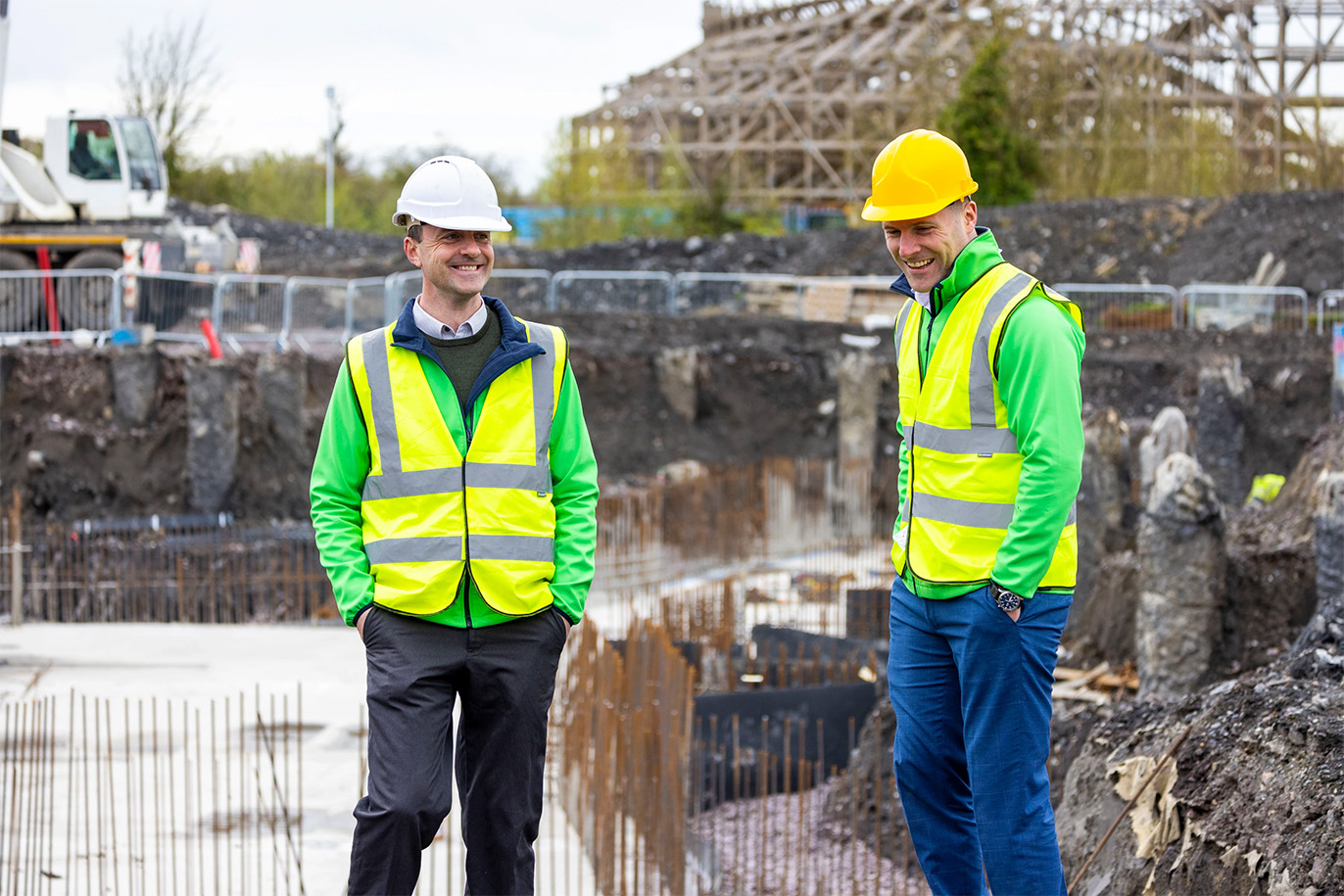 a construction site with two men smiling and a rollercoaster in the back