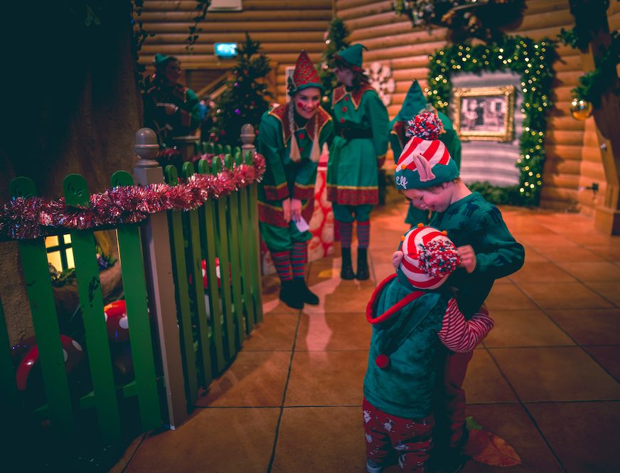 two children dressed as Christmas elves hugging each other