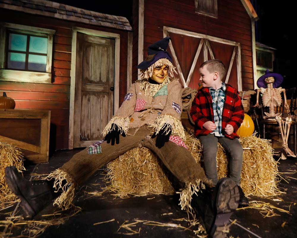 a scarecrow sitting on hay bales with a little boy beside him at an Emerald Park Halloween event