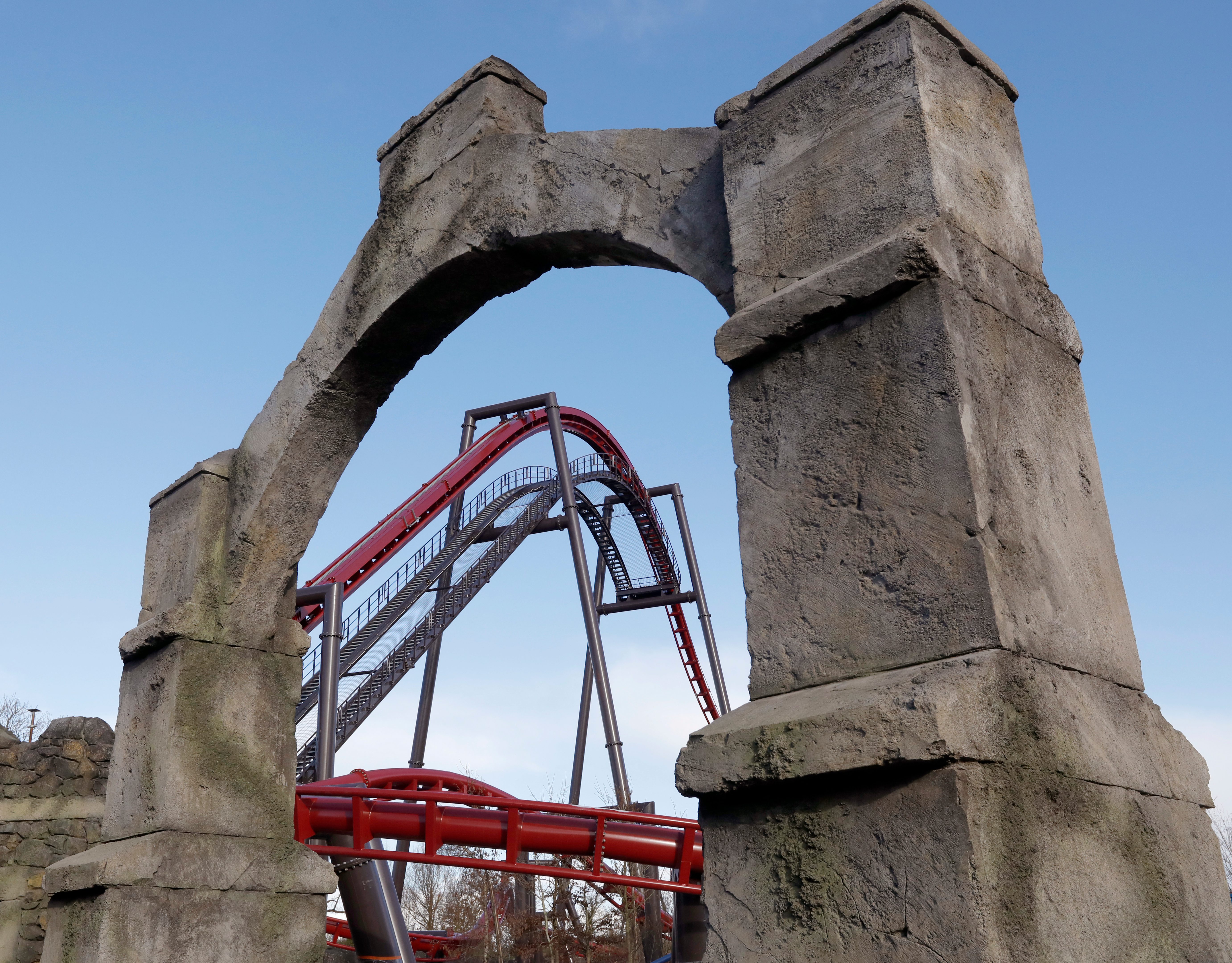 a red rollercoaster lift hill shot through a stone archway